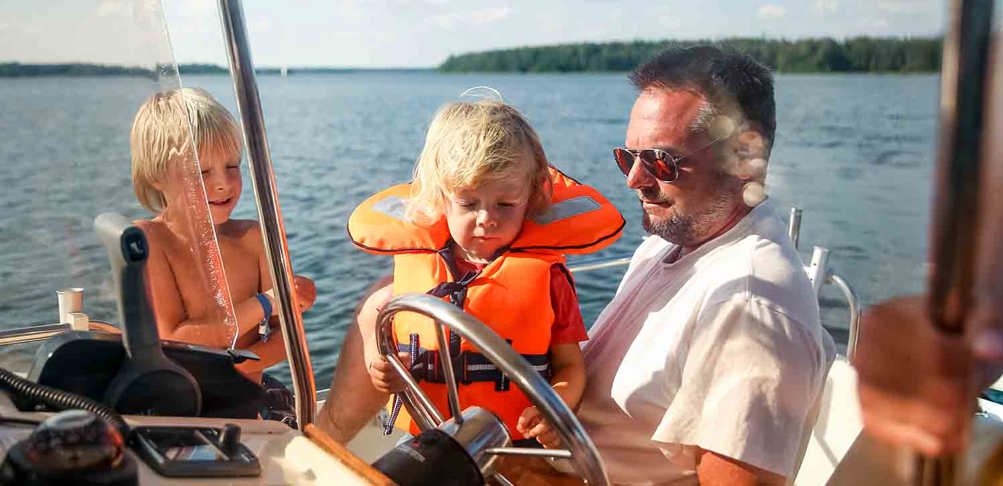 Familj som sitter på en båt en solig sommardag.