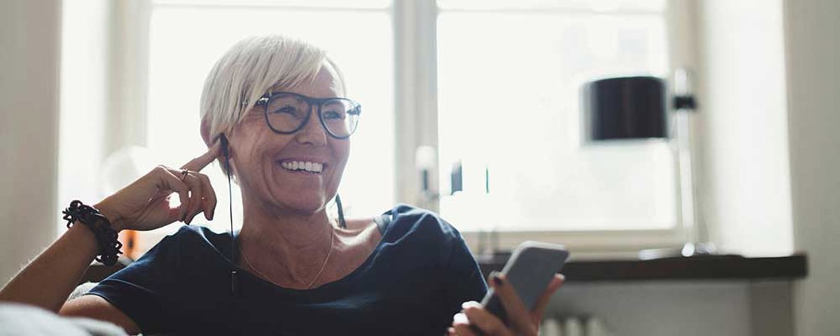 Person med hörlur som sitter och ler med en mobiltelefon i handen