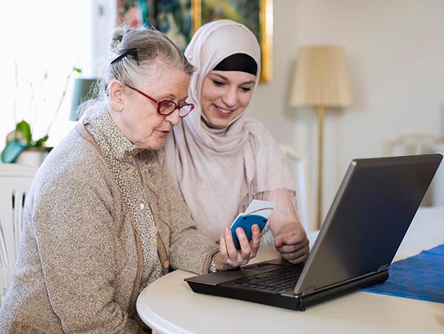 Två kvinnor sitter och tittar gemensamt i en dator.
