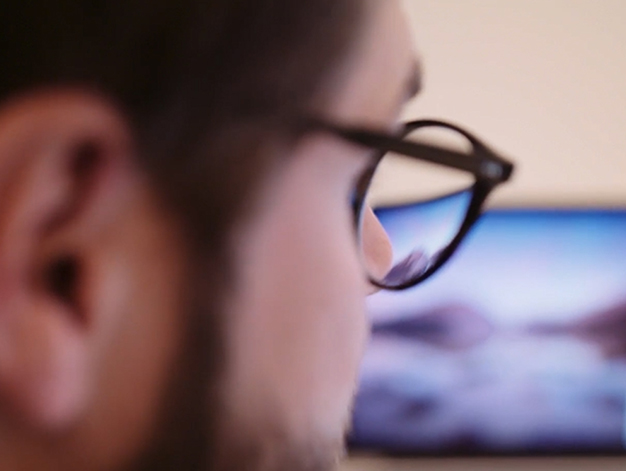 Närbild på man med glasögon som sitter framför en datorskärm.