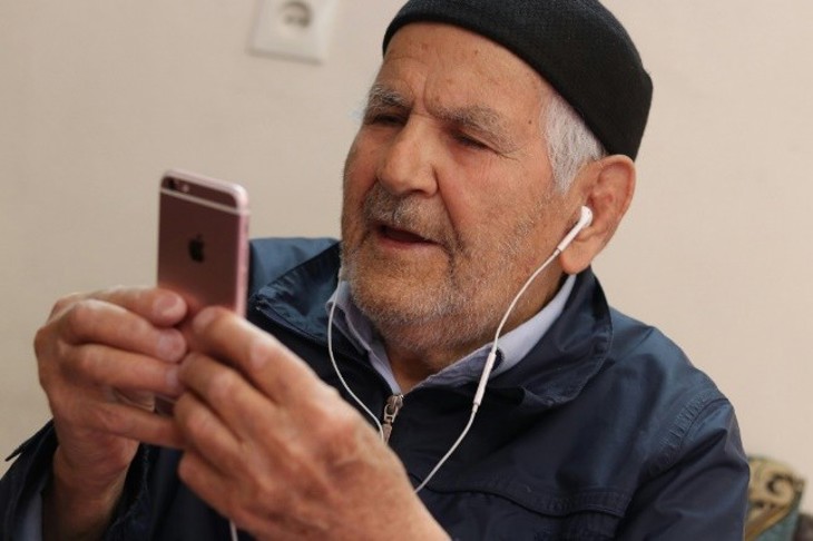 Äldre man med hörlurar tittar i en mobiltelefon
