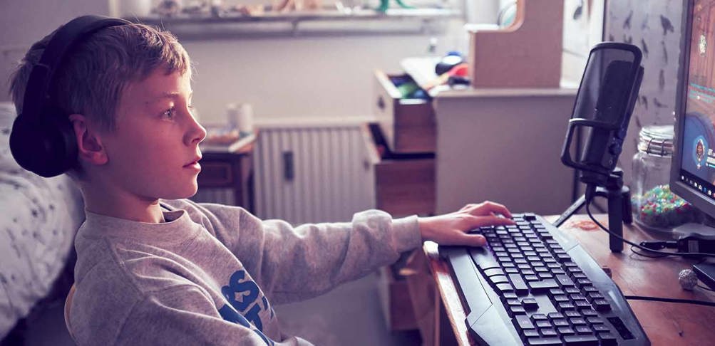 Ung kille sitter och tittaar på datorskärm med händerna på tangentbordet